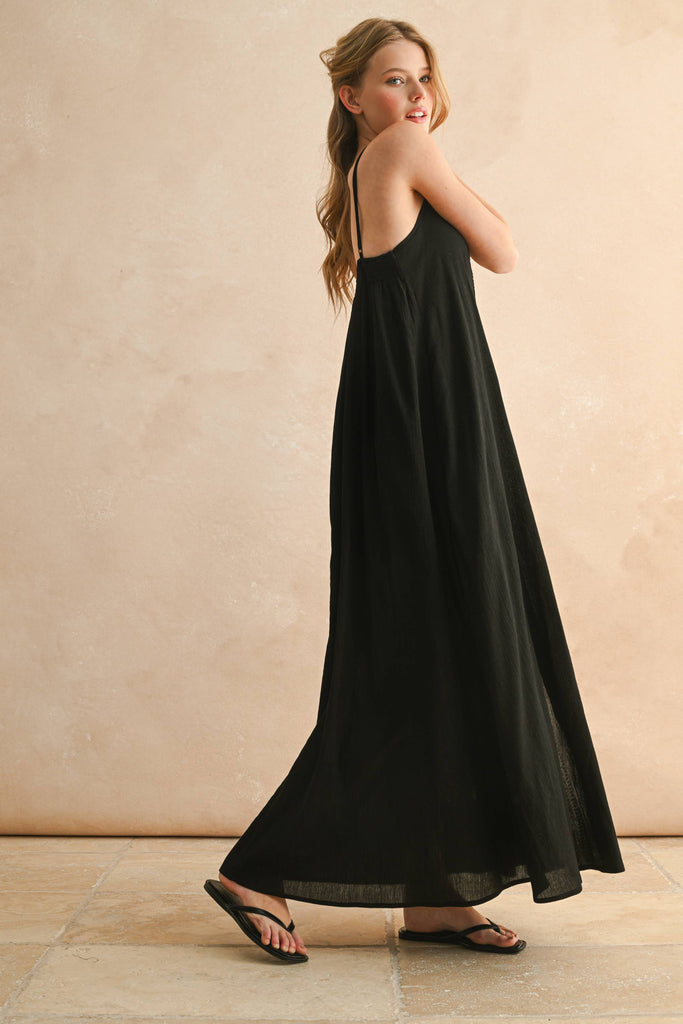 Model in black embroidered maxi dress with thin straps and flowy silhouette, featuring beige V-shaped stitching detail.