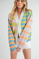 Woman wearing a colorful striped cardigan in pink, blue, green, orange, and lilac with a button-front closure.