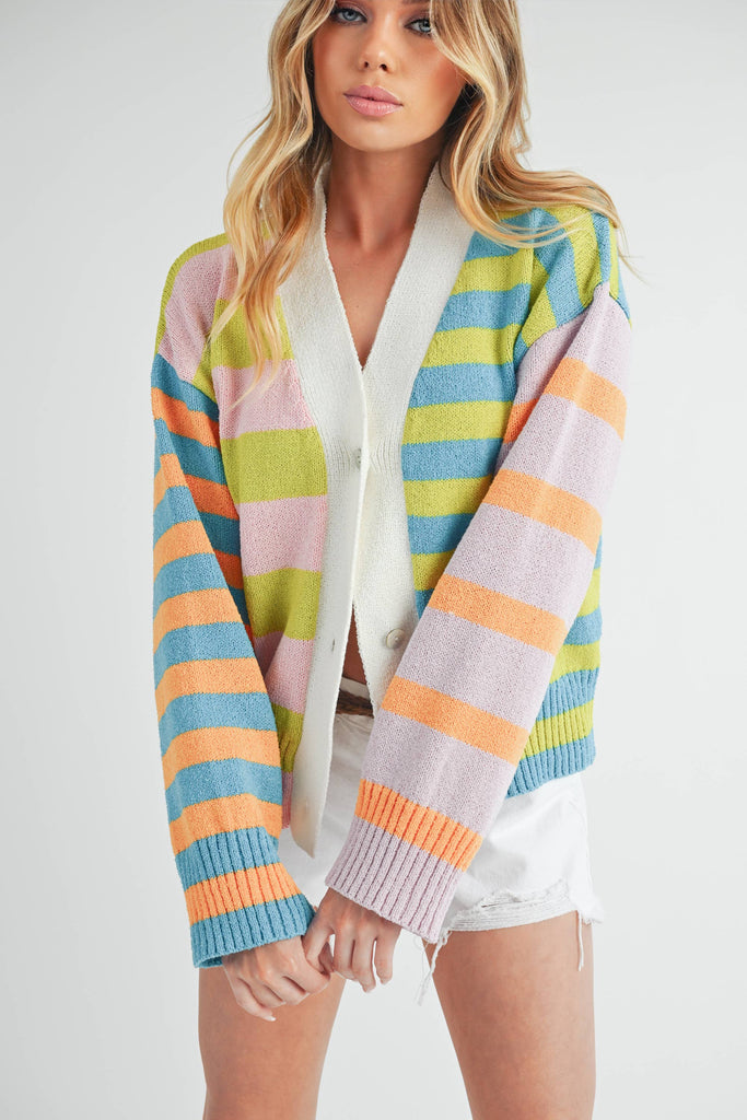 Woman wearing a colorful striped cardigan in pink, blue, green, orange, and lilac with a button-front closure.