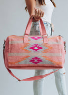 Woman holding a pink and orange woven weekender duffel bag with fuchsia geometric design