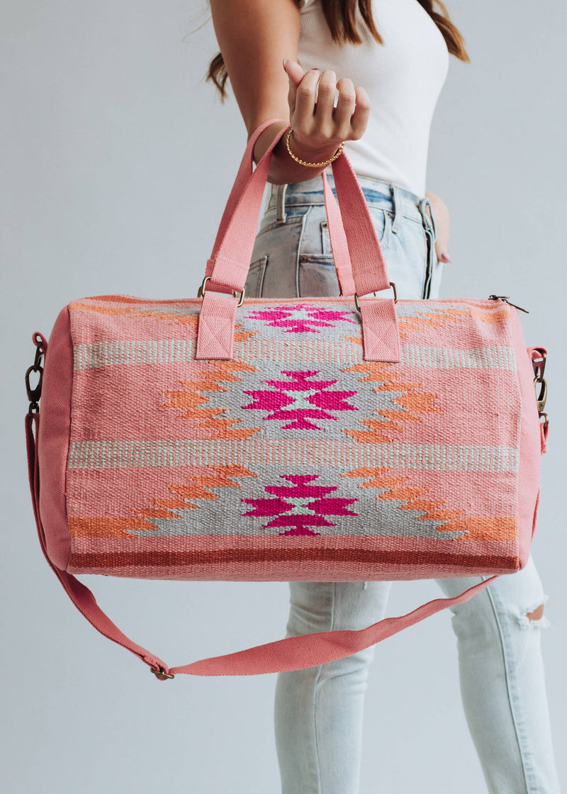 Woman holding a pink and orange woven weekender duffel bag with fuchsia geometric design