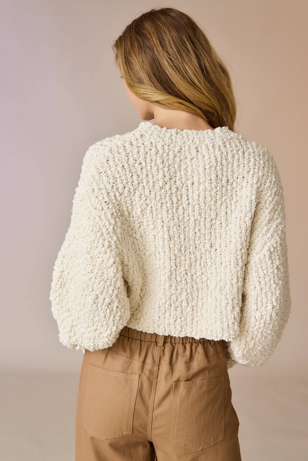 Woman wearing a cream popcorn knit cropped sweater with tan drawstring pants, hands in pockets.