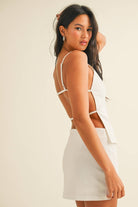 White two-piece set with square-neck top, open back detail, and matching mini skirt with slit, worn by model