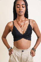 Model wearing a scalloped-edge lace bralette in burgundy and blue tones, styled with layered necklaces and velvet pants.