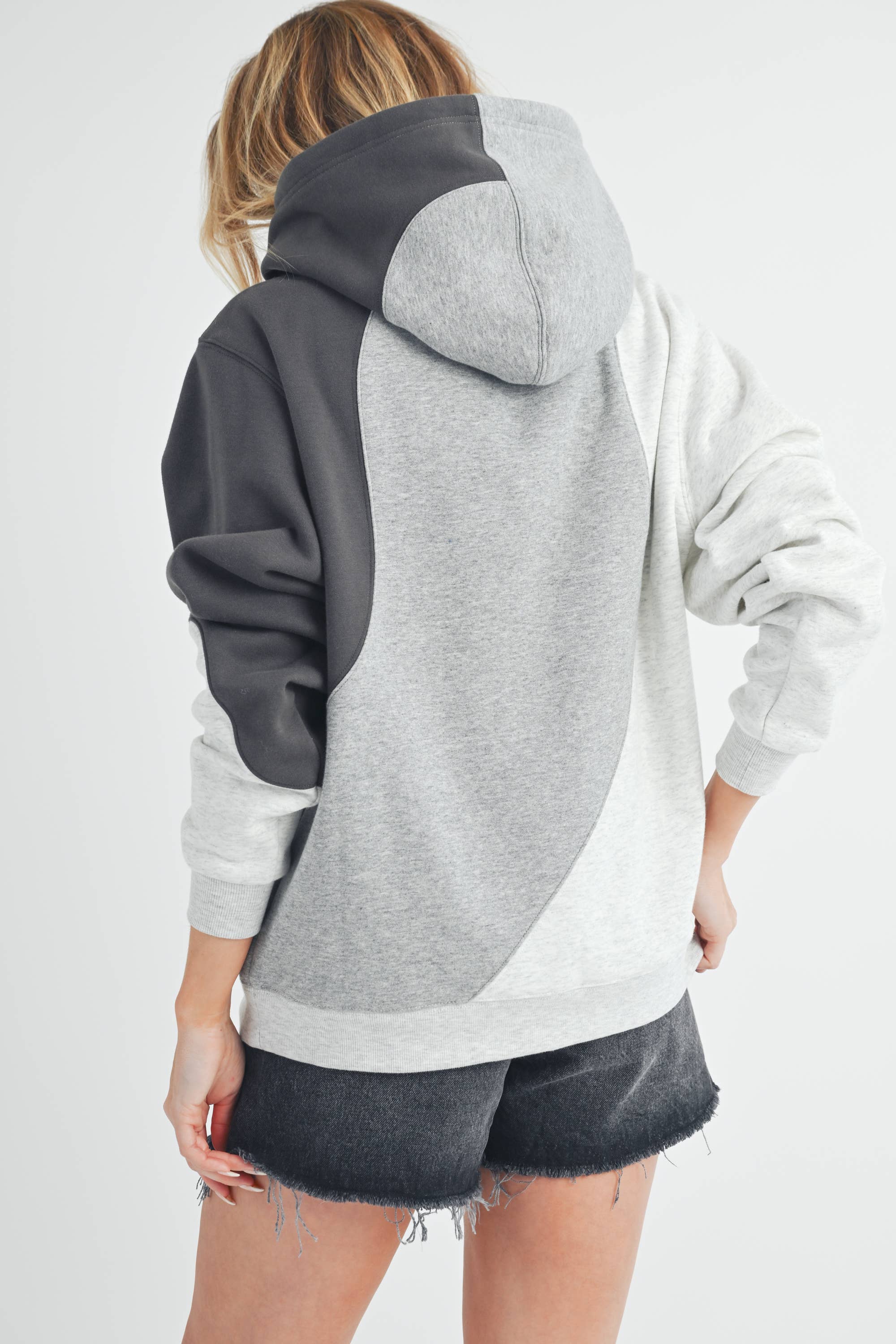 Woman wearing an oversized colorblock hoodie in grey, black, and ivory with a relaxed fit and kangaroo pocket.