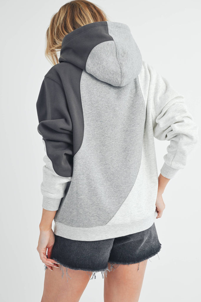Woman wearing an oversized colorblock hoodie in grey, black, and ivory with a relaxed fit and kangaroo pocket.