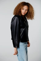 Person wearing a black leather jacket and light blue jeans on a plain background