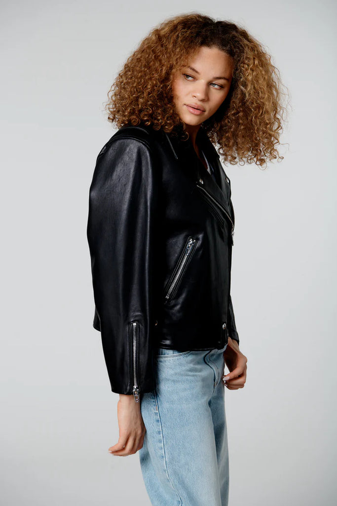 Person wearing a black leather jacket and light blue jeans on a plain background