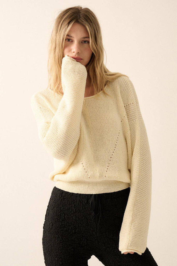 Woman wearing a cream lightweight knit sweater with wide sleeves and a cropped fit.
