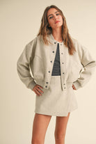 Model wearing a wool-blend jacket and mini skirt set in a neutral tone, styled with a striped tee and relaxed fit, showcasing casual elegance.