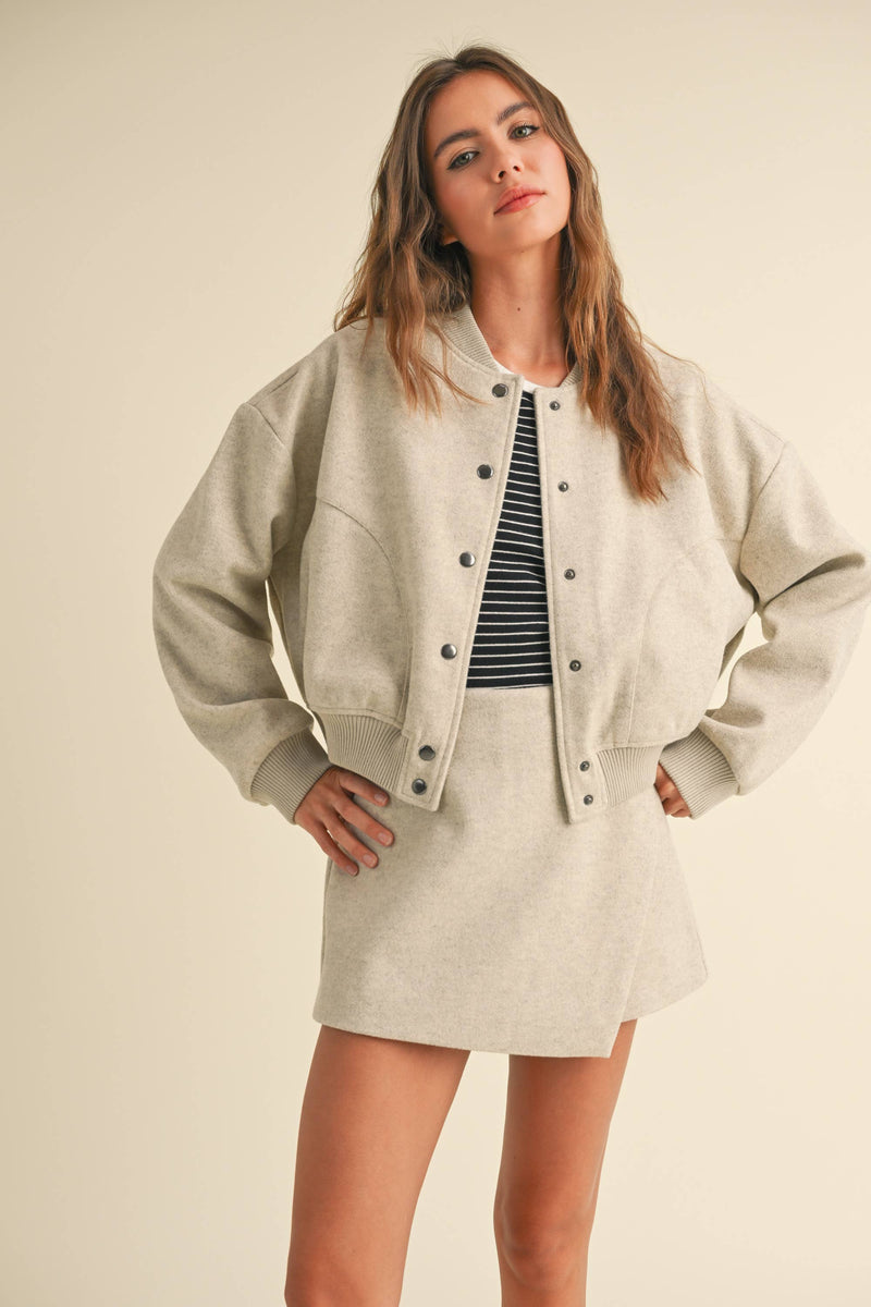 Model wearing a wool-blend jacket and mini skirt set in a neutral tone, styled with a striped tee and relaxed fit, showcasing casual elegance.