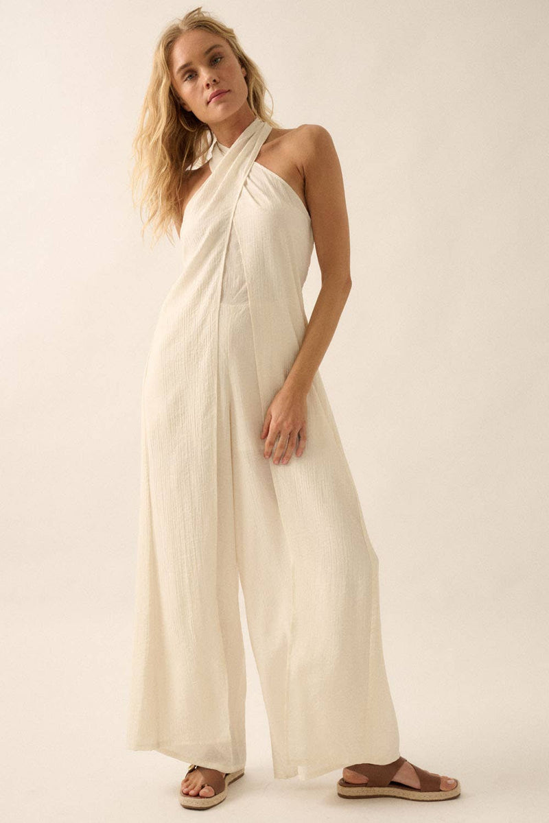 Woman wearing a white halter jumpsuit with tie-back neckline and wide-leg pants, styled with sandals.
