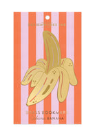 "Cabana Banana" brass metal bookmark in the shape of a peeled banana with an orange and pink striped background.