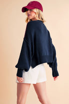 A woman wearing a navy sweater with the text 'USA' in white letters, paired with white shorts and a red cap.