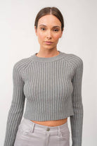 Woman wearing a gray mock neck long sleeve rib knit cropped sweater.