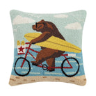 Hook pillow showing a bear in sunglasses riding a red bicycle with a yellow surfboard at the beach, sky and ocean in the background.