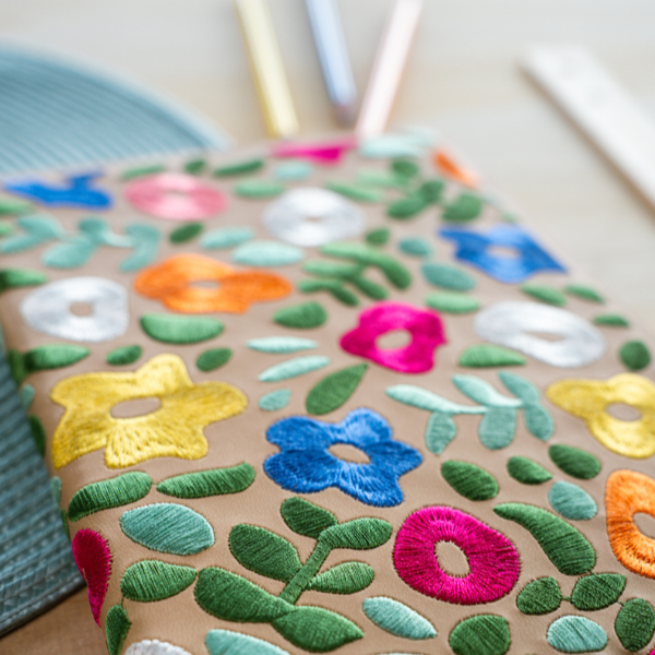 Colorful floral embroidery on a fabric surface with tools in the background