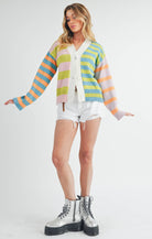 Woman wearing a colorful striped cardigan in pink, blue, green, orange, and lilac with a button-front closure.