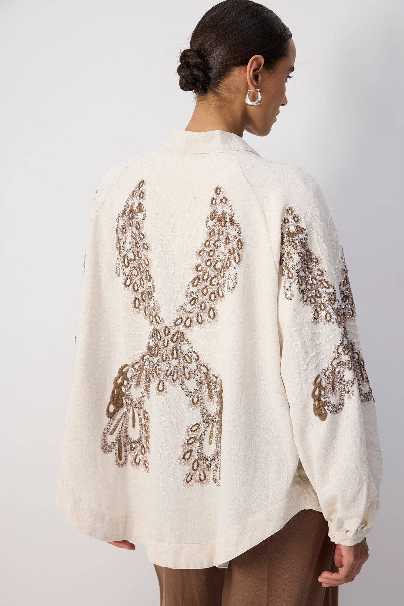 Back view of a woman wearing a cream embroidered kimono with sequin detailing and wide sleeves.