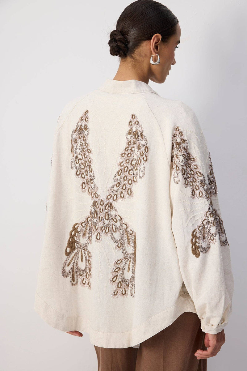 Back view of a woman wearing a cream embroidered kimono with sequin detailing and wide sleeves.