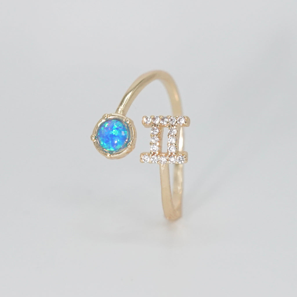 Gemini Ring: Twin symbols with shimmering stones surrounding an opal, symbolizing duality.