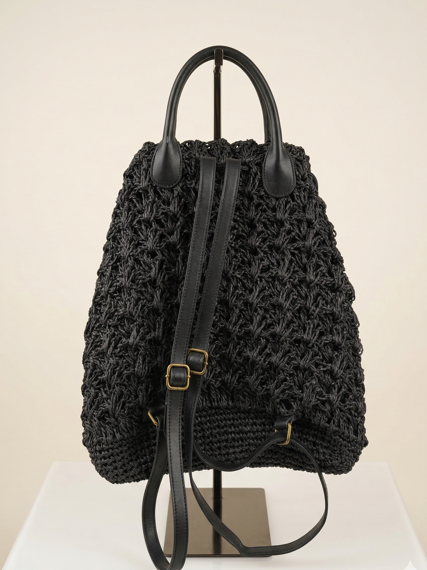 Black woven backpack with leather straps on a white surface