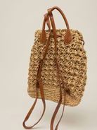 Woven straw backpack with brown leather straps on a light beige background