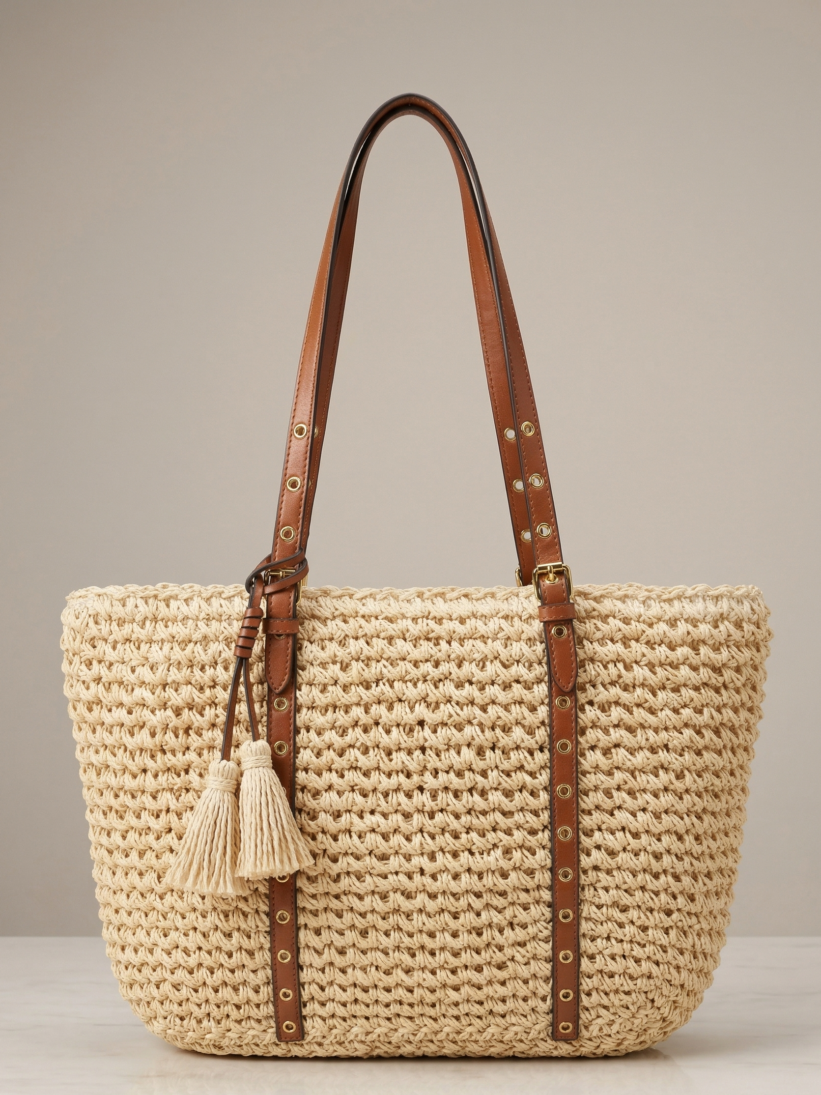 Woven straw handbag with brown straps and tassel on a neutral background