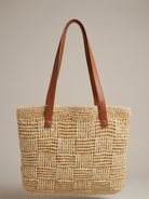 Woven straw tote bag with brown leather handles on a beige background