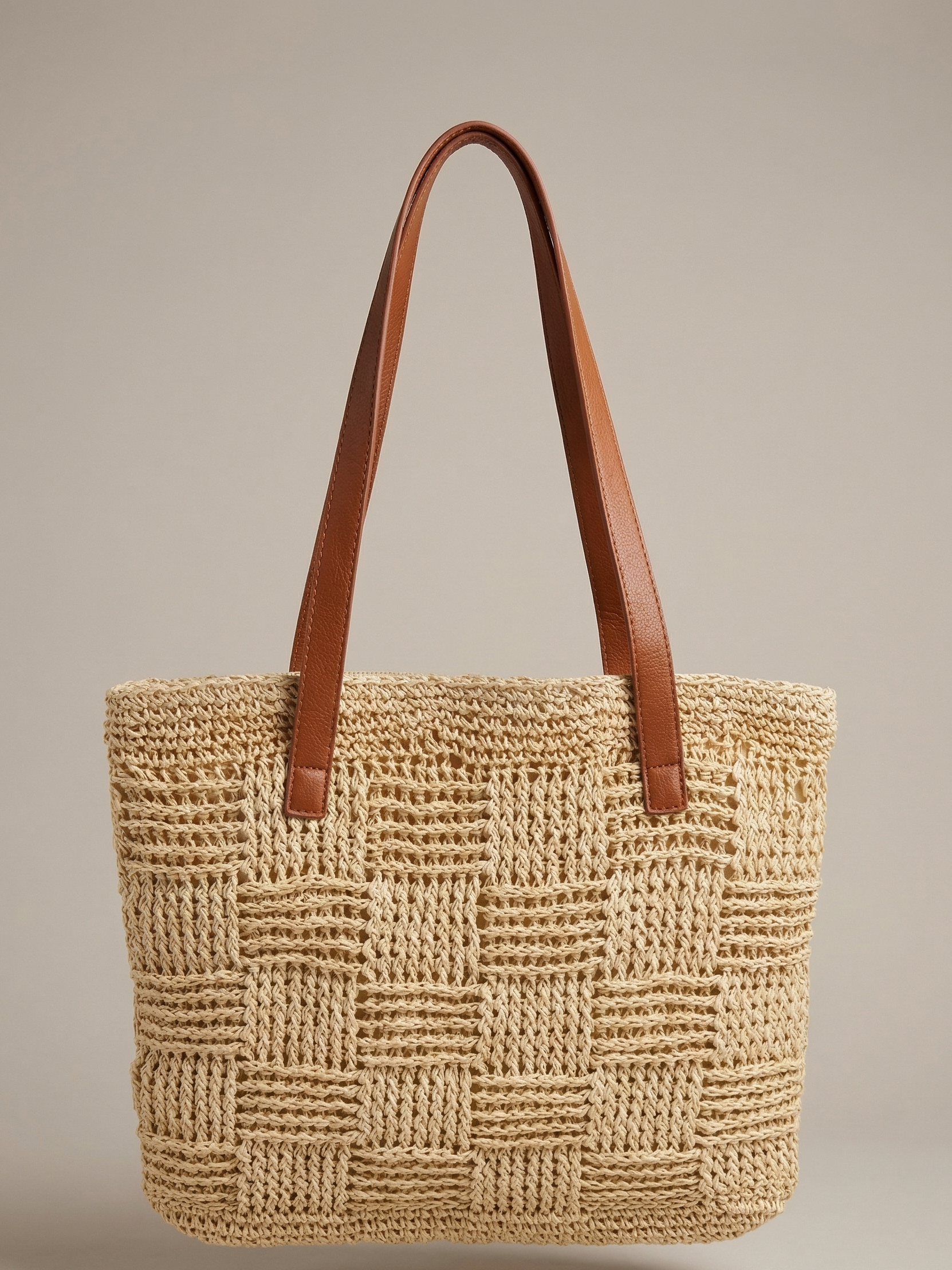 Woven straw tote bag with brown leather handles on a beige background