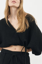 Siena Top displayed on a hanger, showcasing its wide sleeves and the unique V-shaped front drape with a hidden optional closure.