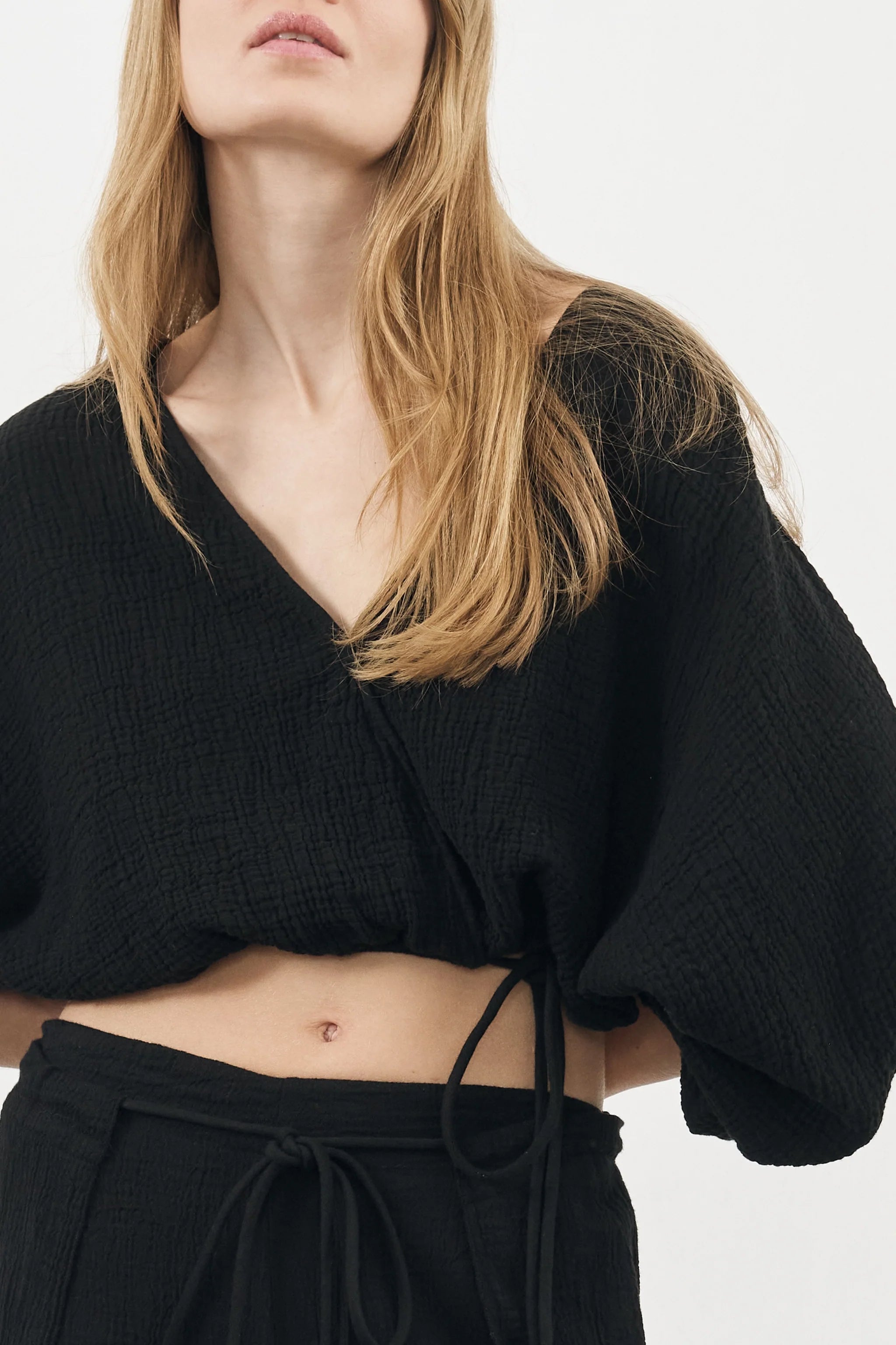 Siena Top displayed on a hanger, showcasing its wide sleeves and the unique V-shaped front drape with a hidden optional closure.