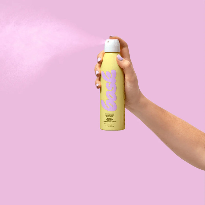 Hand holding Bask SPF 50 Sunscreen Spray, showing the spray function against a sunny beach scene.