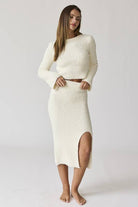 Woman wearing a white round neck long sleeve crop soft knit top and midi skirt set with a side slit.