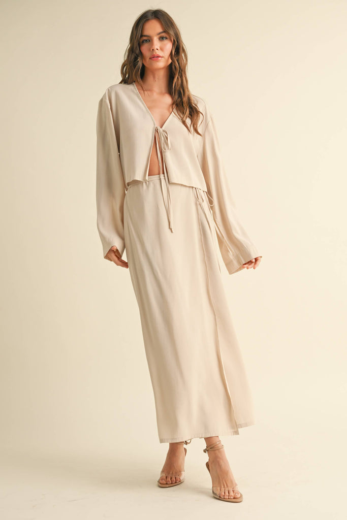 Woman wearing a beige tie-front long sleeve top and matching wrap maxi skirt, styled as a coordinated skirt set.