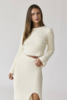 Woman wearing a white round neck long sleeve crop soft knit top and midi skirt set with a side slit.