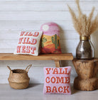 Colorful hooked pillow shaped with a desert scene, featuring cacti, sun, and sunset tones in pink, orange, and yellow.