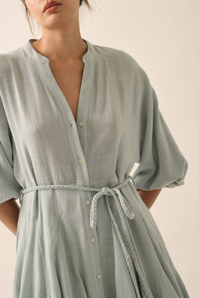 Woman wearing a sage green button-down mini dress with a braided waist tie and flowy hemline.