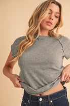 Woman wearing a gray short sleeve tee tucked into a dark wash denim mini skirt with slide sandals, posing in front of a neutral background.