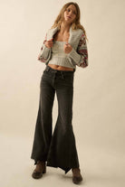 Woman wearing a patterned cardigan, crop top, and flared jeans on a beige background