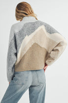 Front and back view of a woman wearing a color-block knit sweater in grey, cream, and taupe with a relaxed fit.