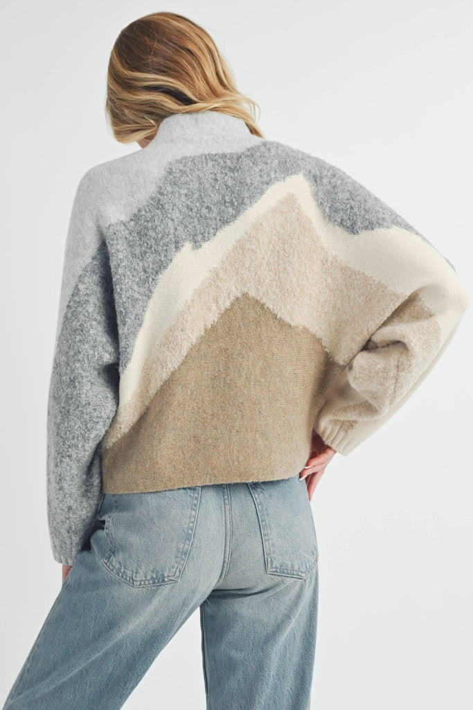 Front and back view of a woman wearing a color-block knit sweater in grey, cream, and taupe with a relaxed fit.