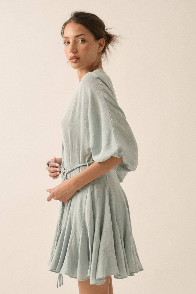 Woman wearing a sage green button-down mini dress with a braided waist tie and flowy hemline.