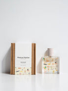 Maison Matine Bain de Midi perfume bottle with playful illustrations and white cap, styled with flowers and modern props.