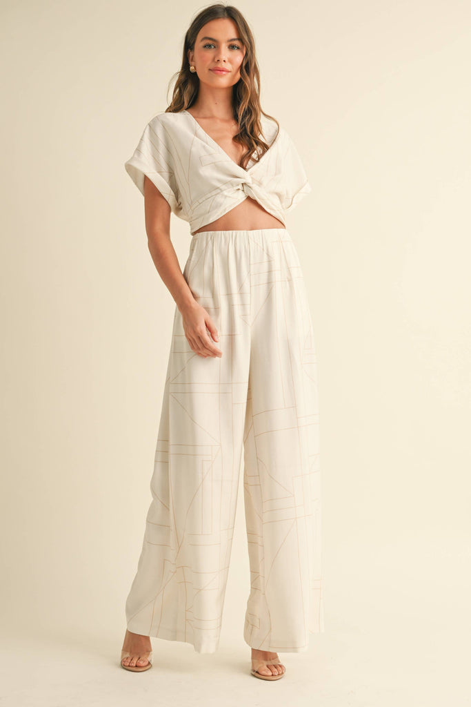 Woman wearing a cream two-piece set with geometric line print, knotted crop top, and wide-leg pants.