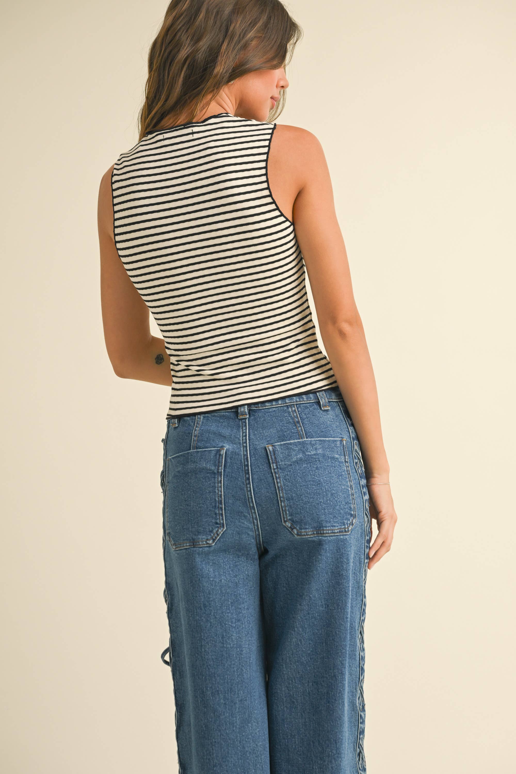 Striped knit tank top with a scoop neckline and ruched bust, styled with high-waisted denim for a casual yet chic look.