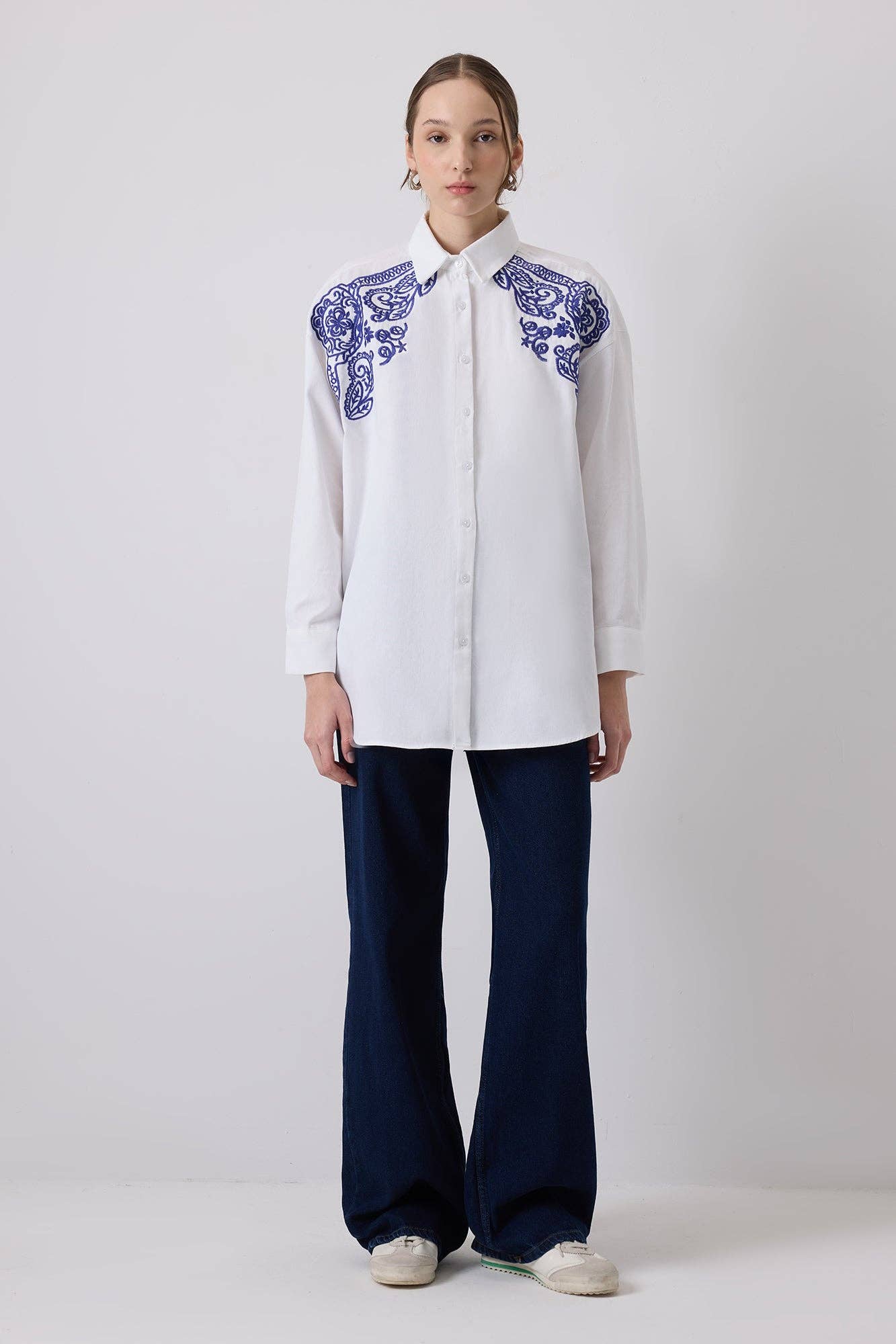 Woman wearing a white oversized shirt with bold blue embroidery on shoulders