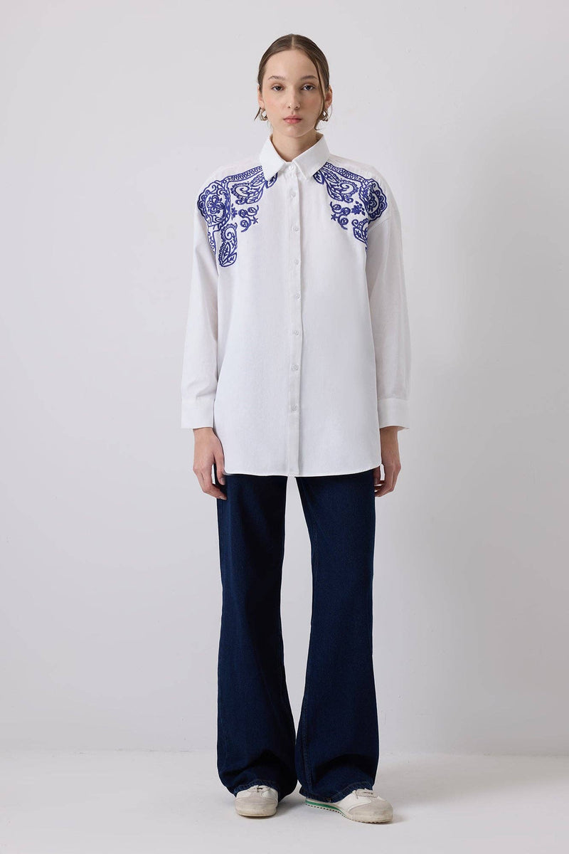 Woman wearing a white oversized shirt with bold blue embroidery on shoulders