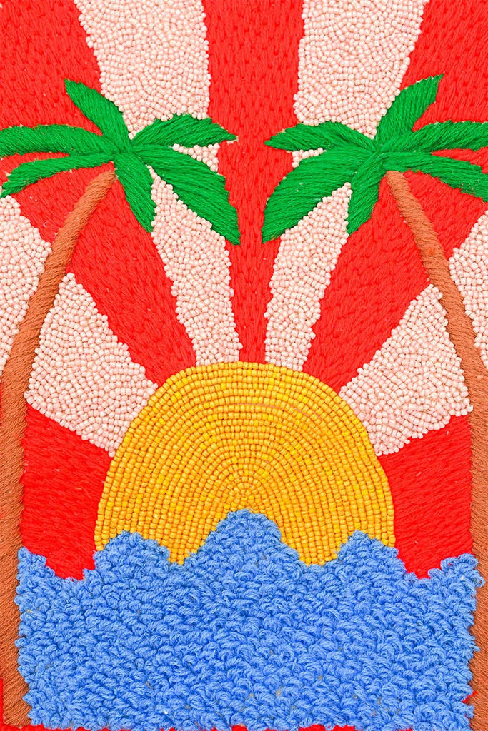 Beaded tote bag with sunset, palm tree, and ocean design, featuring black stripes, colorful pom-pom trim, and long handles.