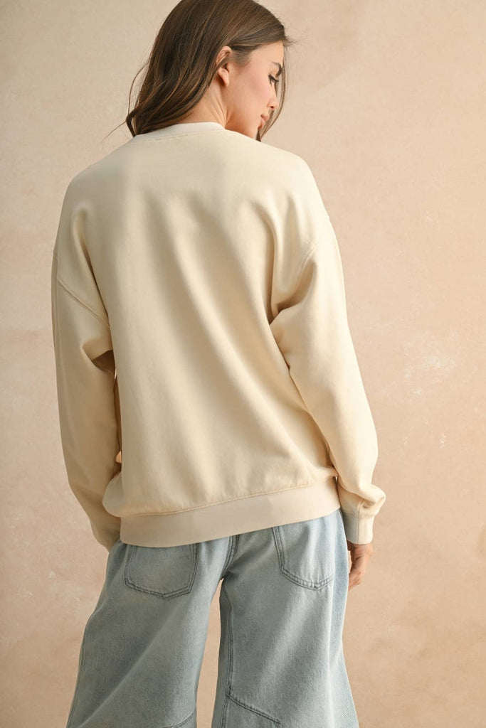 Woman wearing a cream sweater with a textured rope-stripe American flag design, paired with light wash jeans.